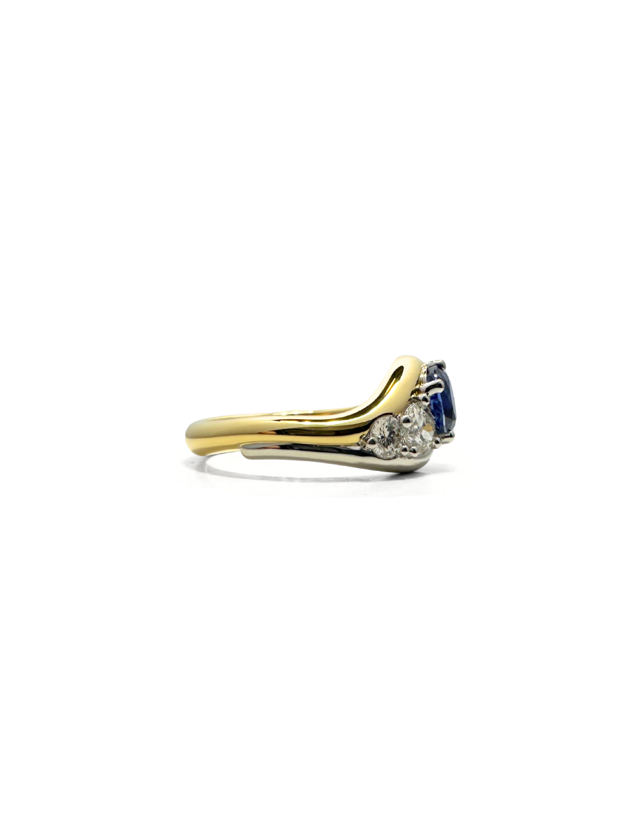Side view of a custom Gold ring with a blue sapphire and diamonds on a white background