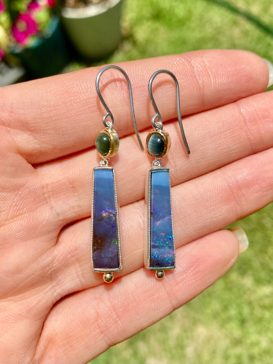 hand holing a pair of earrings with green tourmaline and blue boulder opal set in yellow gold and silver