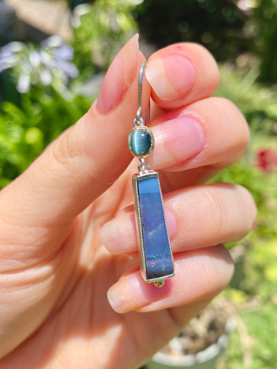 hand holding an earring with green tourmaline and blue boulder opal set in yellow gold and silver