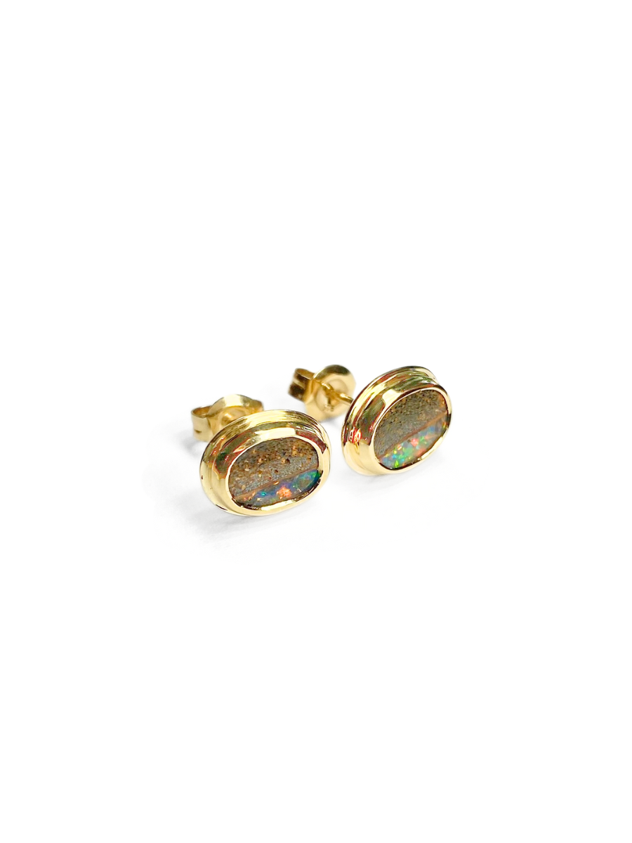 Pair of gold, bezel set earrings with opal stones on a white background. Opals include ironstone inclusions and a rainbow, glittery strip of opal