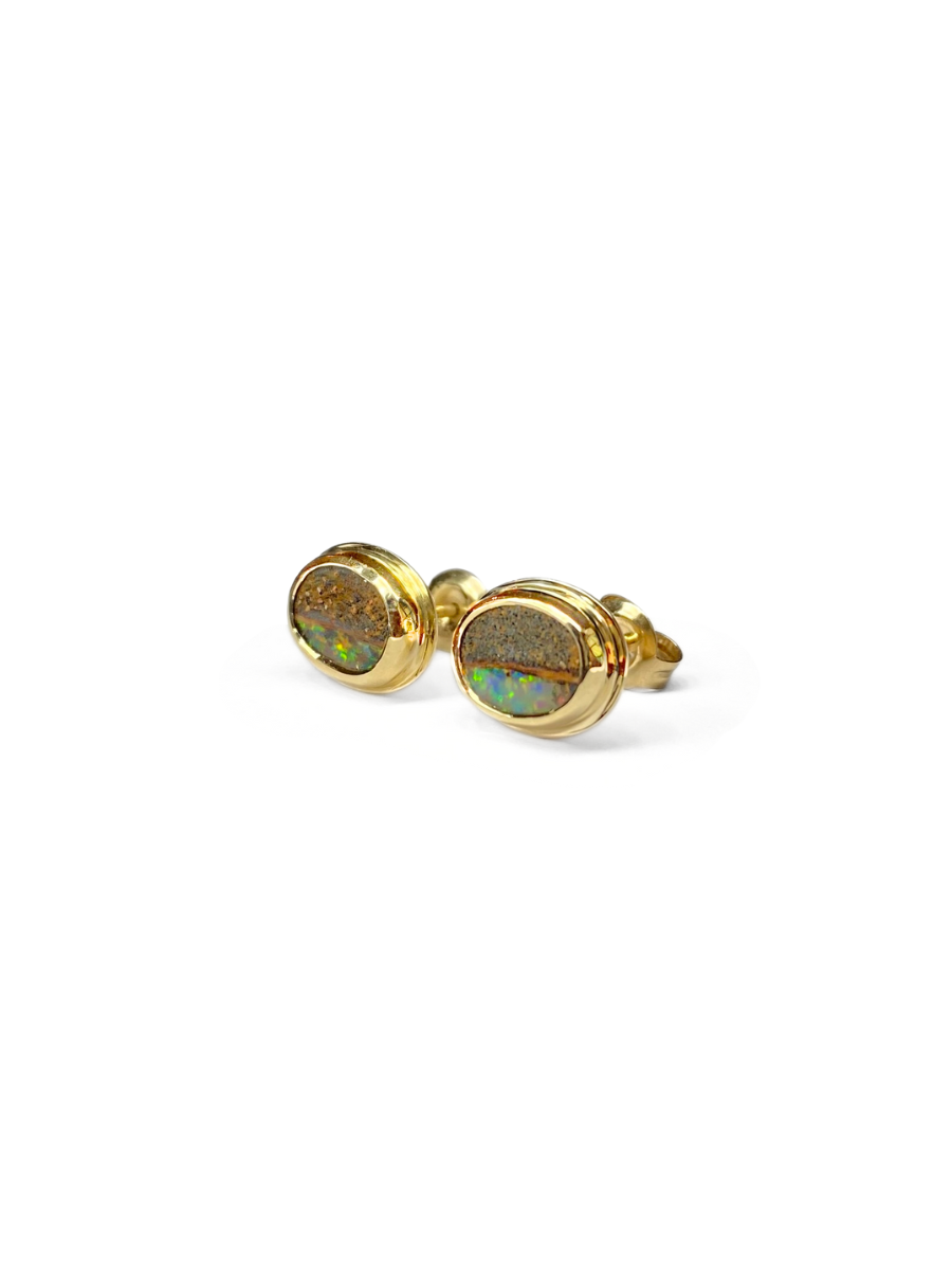 Pair of gold, bezel set earrings with opal stones on a white background. Opals include ironstone inclusions and a rainbow, glittery strip of opal