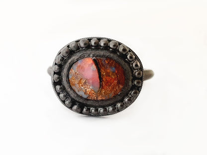 Queensland Boulder Opal ring with a blackedned silver bezel framed by silver balls. This opal looks like a dragons eye, the stone can be seen through the colours of the opal. The opal has reds blue greens and purples. Hand crafted and Australian made by Custom Jewellery Co using local and ethically sourced materials. Australian designed and made for high quality fine jewellery. 