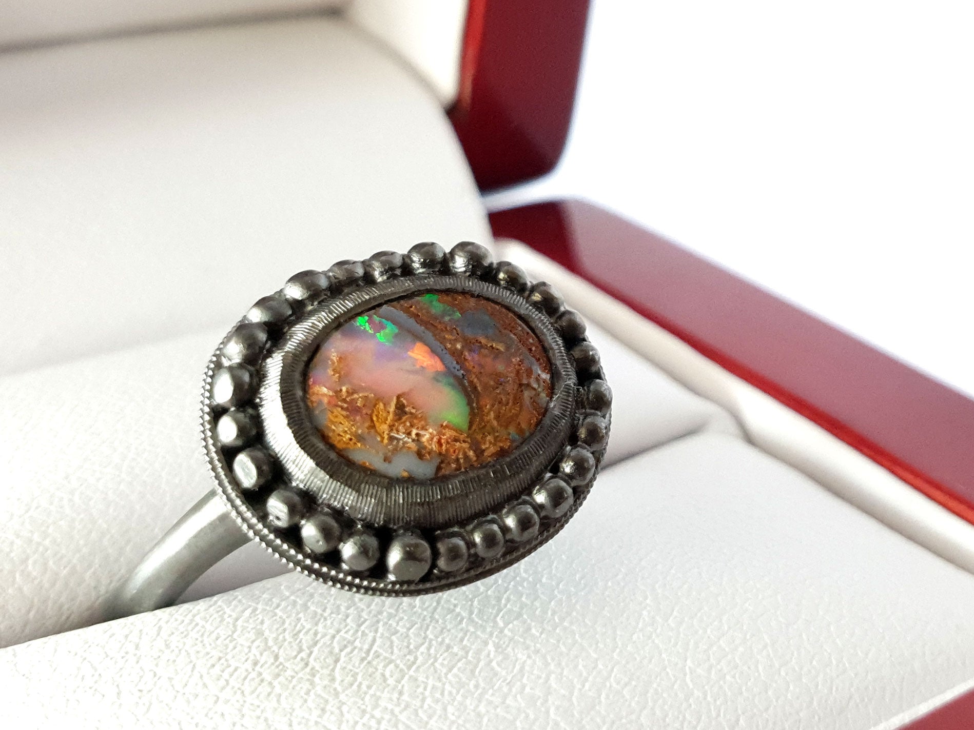 Queensland Boulder Opal ring with a blackedned silver bezel framed by silver balls. This opal looks like a dragons eye, the stone can be seen through the colours of the opal. The opal has reds blue greens and purples. Hand crafted and Australian made by Custom Jewellery Co using local and ethically sourced materials. Australian designed and made for high quality fine jewellery. 