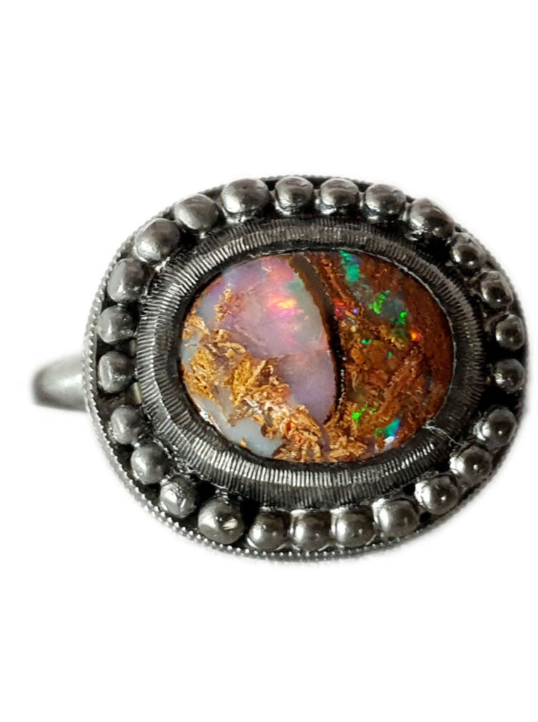Queensland Boulder Opal ring with a blackedned silver bezel framed by silver balls. This opal looks like a dragons eye, the stone can be seen through the colours of the opal. The opal has reds blue greens and purples. Hand crafted and Australian made by Custom Jewellery Co using local and ethically sourced materials. Australian designed and made for high quality fine jewellery. 