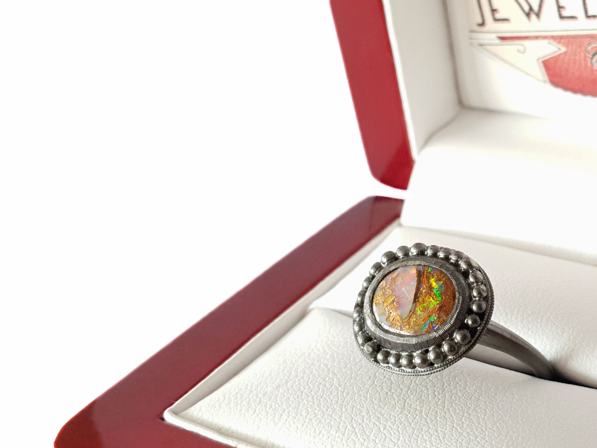 Queensland Boulder Opal ring with a blackedned silver bezel framed by silver balls. This opal looks like a dragons eye, the stone can be seen through the colours of the opal. The opal has reds blue greens and purples. Hand crafted and Australian made by Custom Jewellery Co using local and ethically sourced materials. Australian designed and made for high quality fine jewellery. 