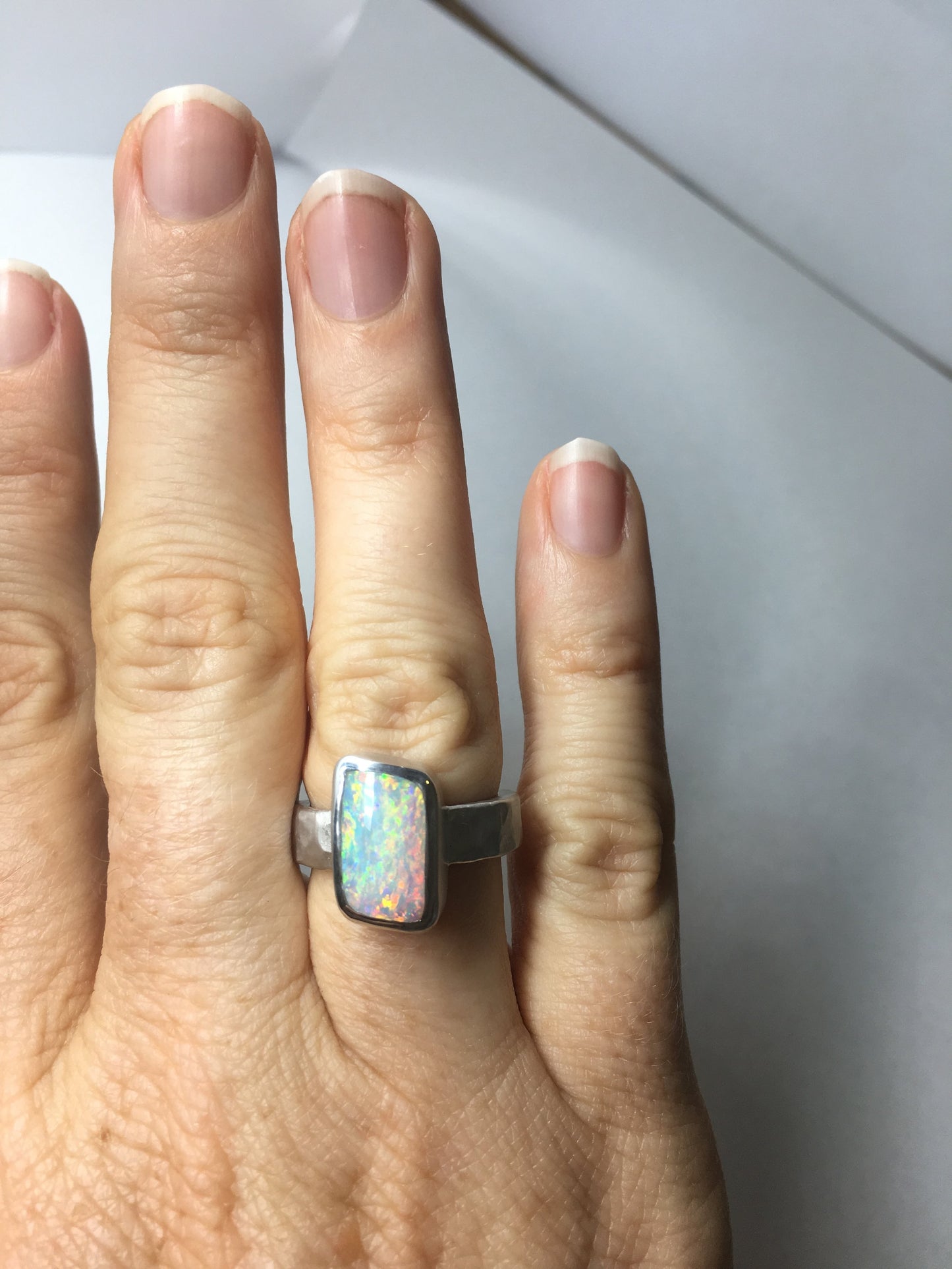 Photo on Hand. Queensland Boulder Opal Sterling Silver Ring. Light opal hand crafted in Brisbane Studio using ethically sourced materials. Wide textured band with a hammered finish. Stone is white pink and green. 